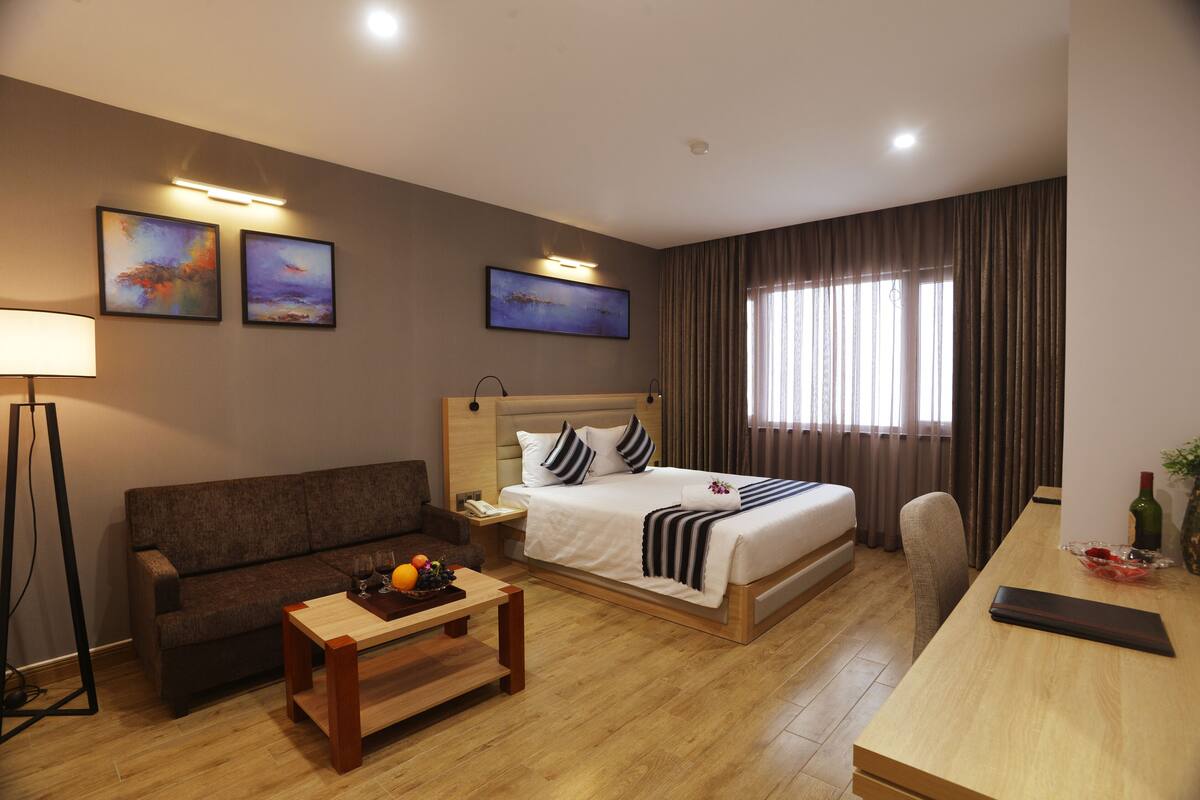 Quarto de hotel com cama, sofá, escrivaninha e abajur.