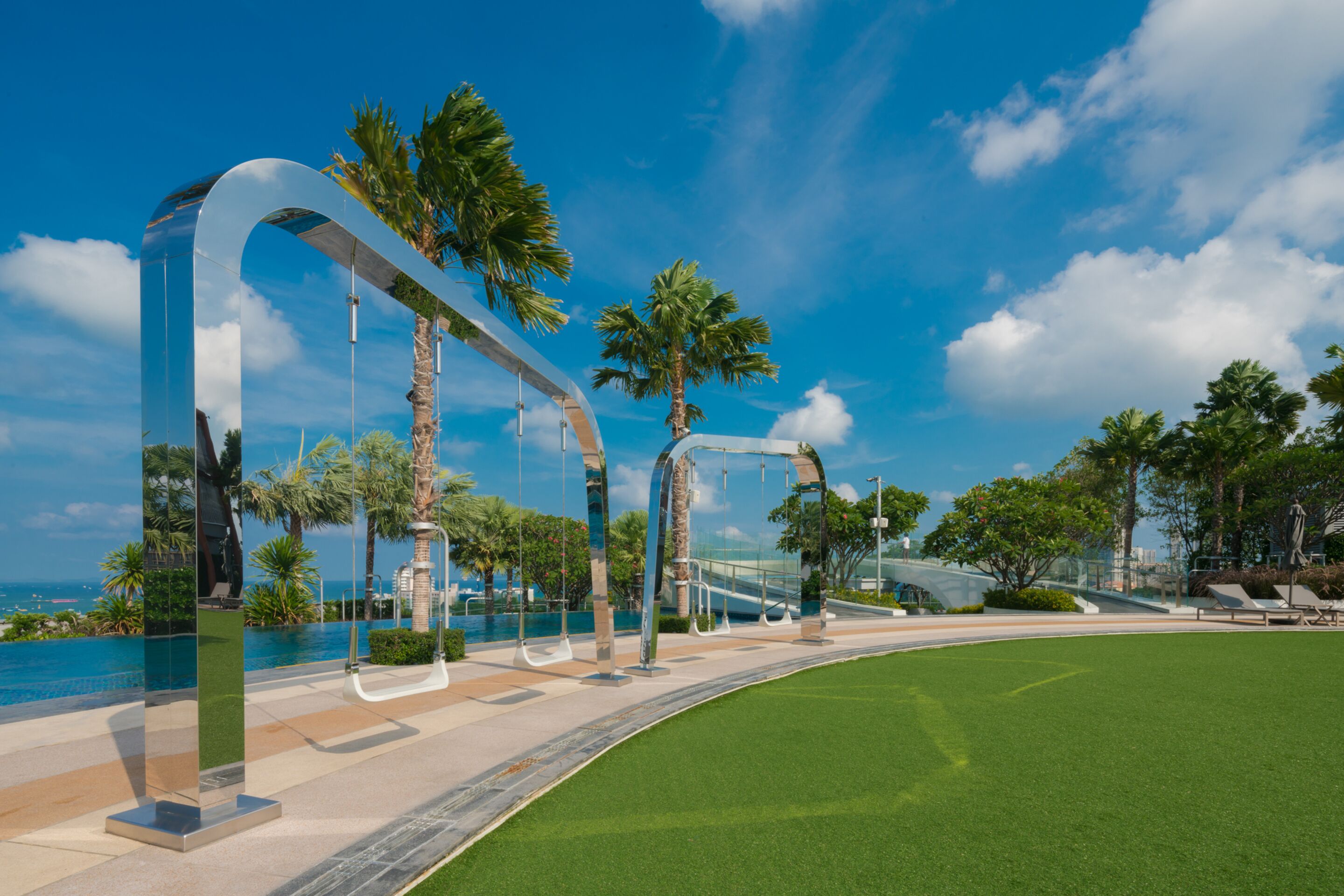 A modern outdoor area with a curved pathway, palm trees, and a clear blue sky.