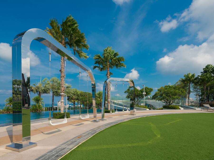 A modern outdoor area with a curved pathway, palm trees, and a clear blue sky.