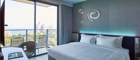Habitación de hotel moderna con una cama grande, un escritorio y una silla. Se aprecia vista de la ciudad a través de amplios ventanales.