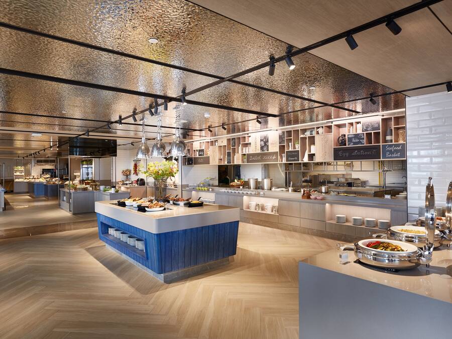 Una cocina moderna con una isla central, diferentes estaciones de comida y un menú en una pizarra.