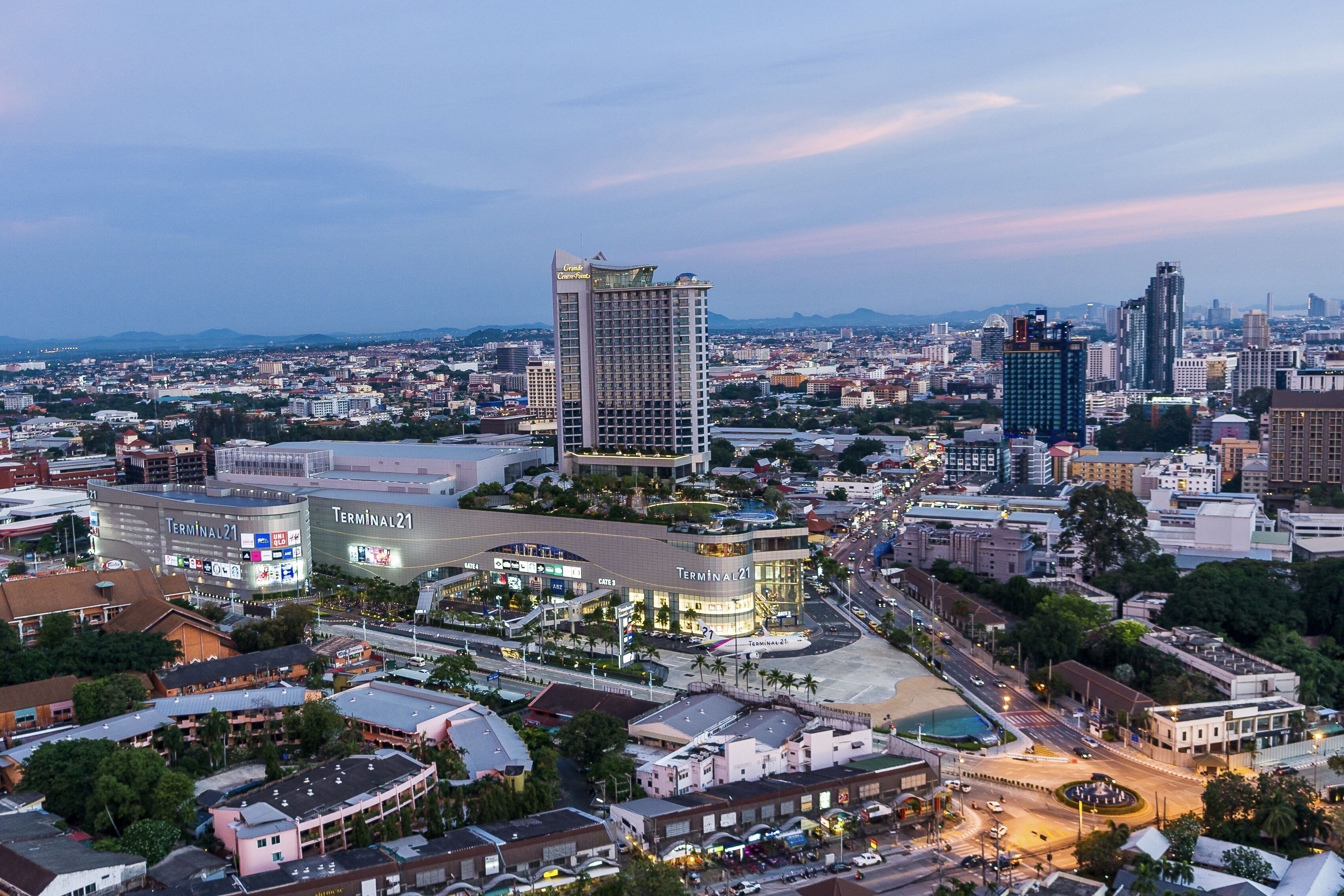 Une vue urbaine mettant en évidence un bâtiment imposant portant l’inscription « Terminal 21 », caractérisé par un design moderne, et entouré d’autres immeubles commerciaux et d’une rue animée.
