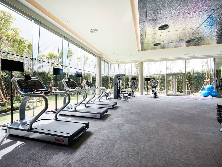 Un gimnasio moderno con cintas de correr, equipo de ejercicio y ventanas amplias que ofrecen vistas a zonas verdes y edificios.