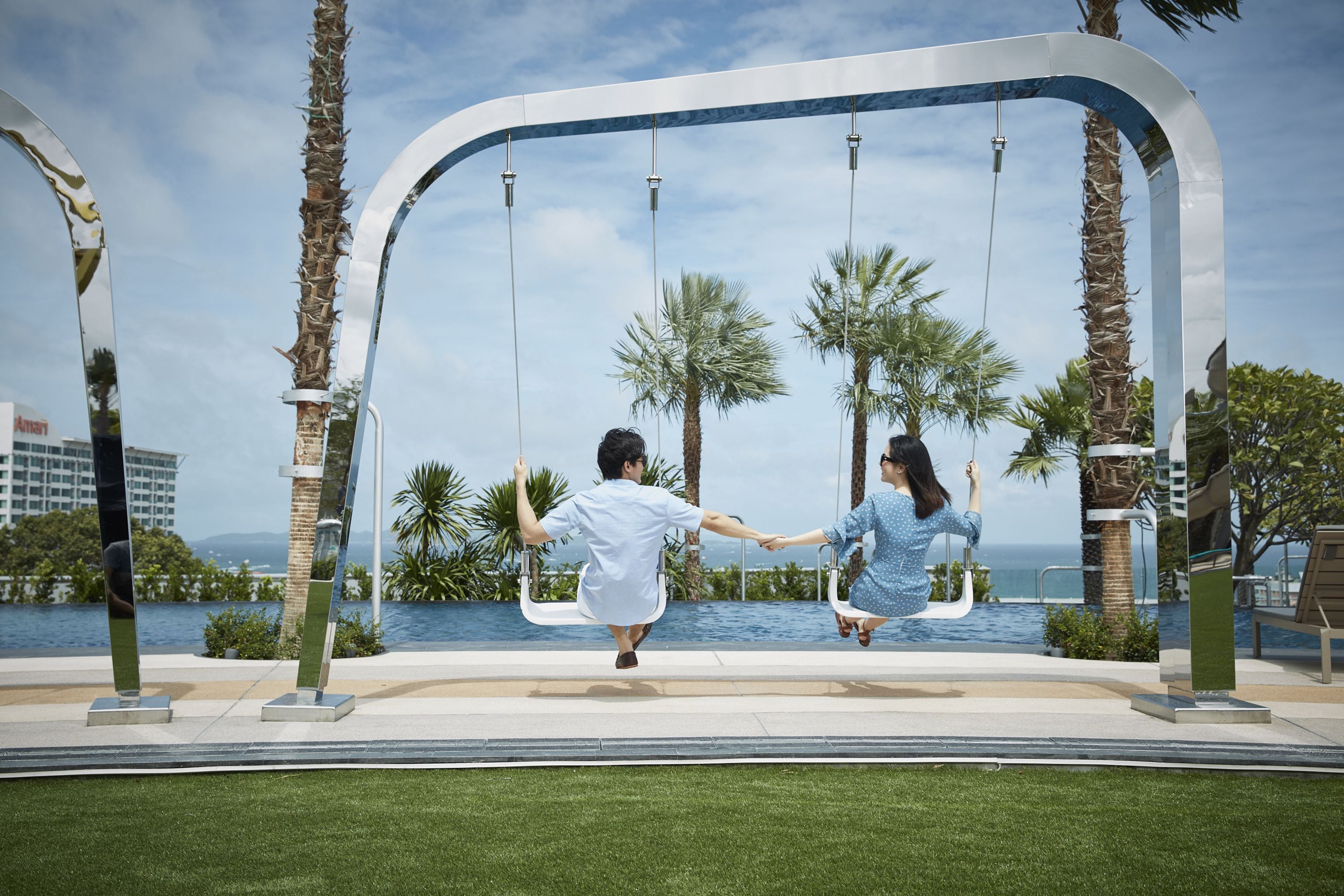 A couple swinging on a modern swing set with a view of the ocean and palm trees.