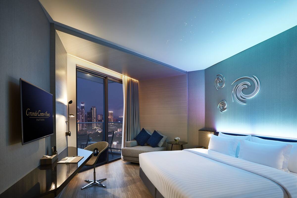A modern hotel room with a large bed, a desk, a chair, and a TV.