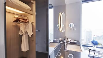 A modern bathroom with a robe hanging on a rack, a vanity with a mirror, and a view of the city through a large window.