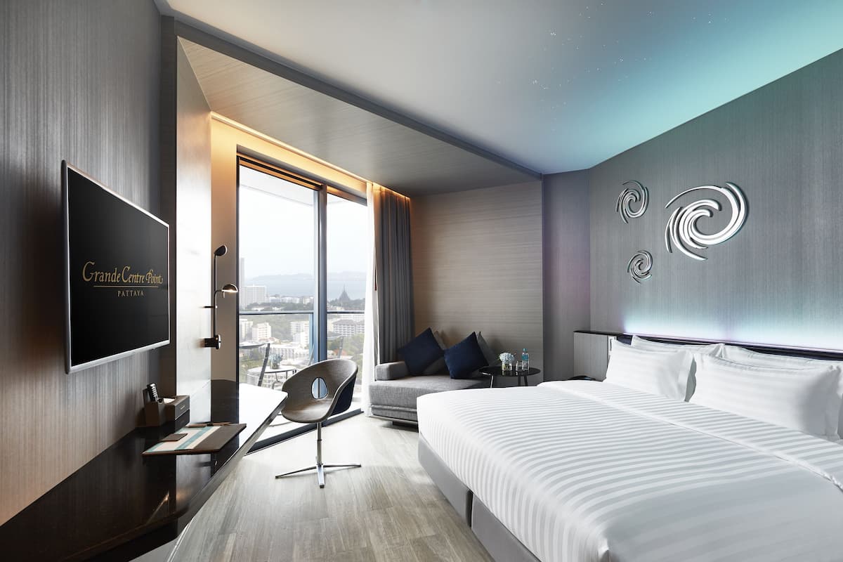 A modern hotel room with a large bed, a TV, a desk, and a view of the city.