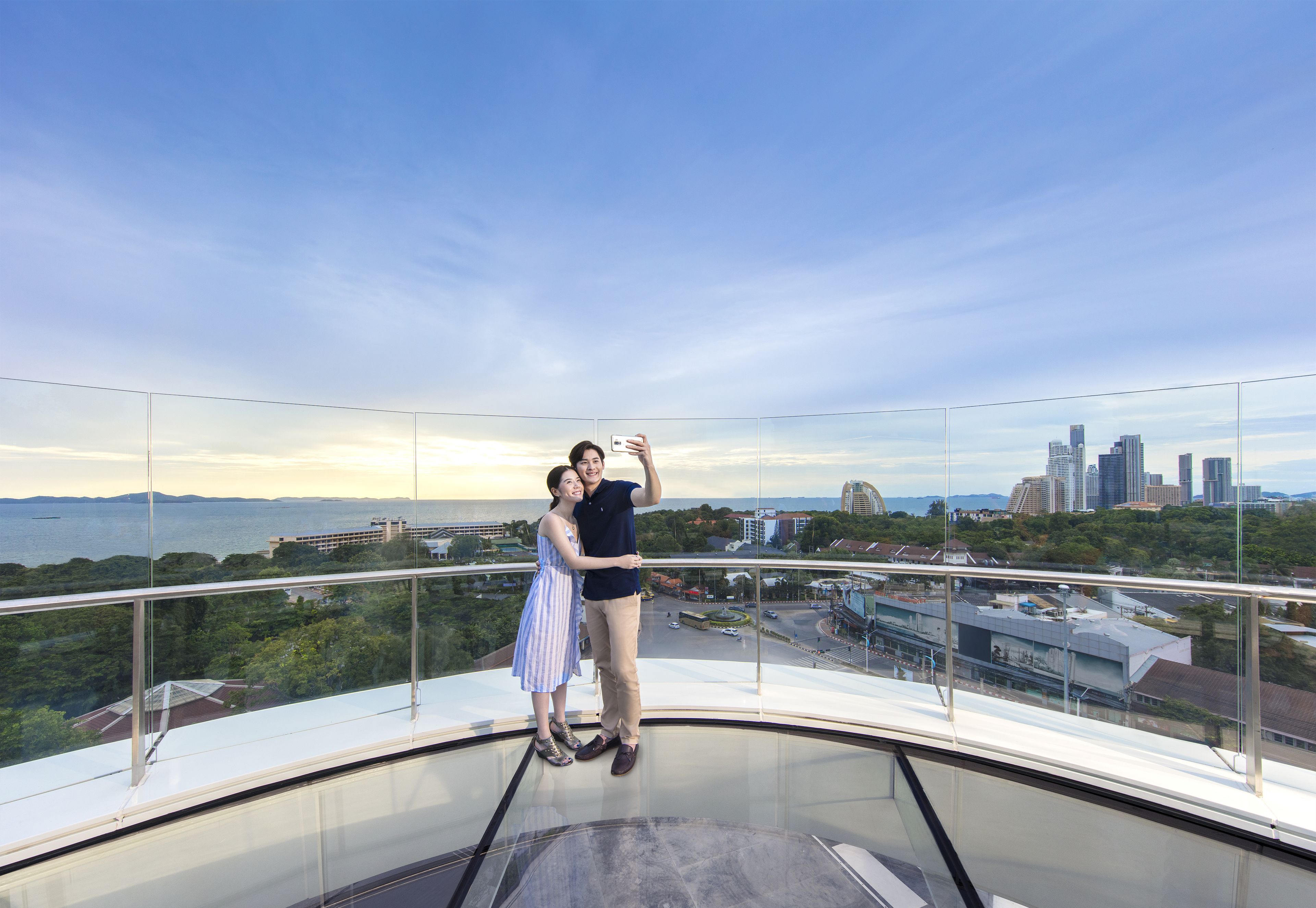 A couple standing on a glass balcony with a cityscape view.