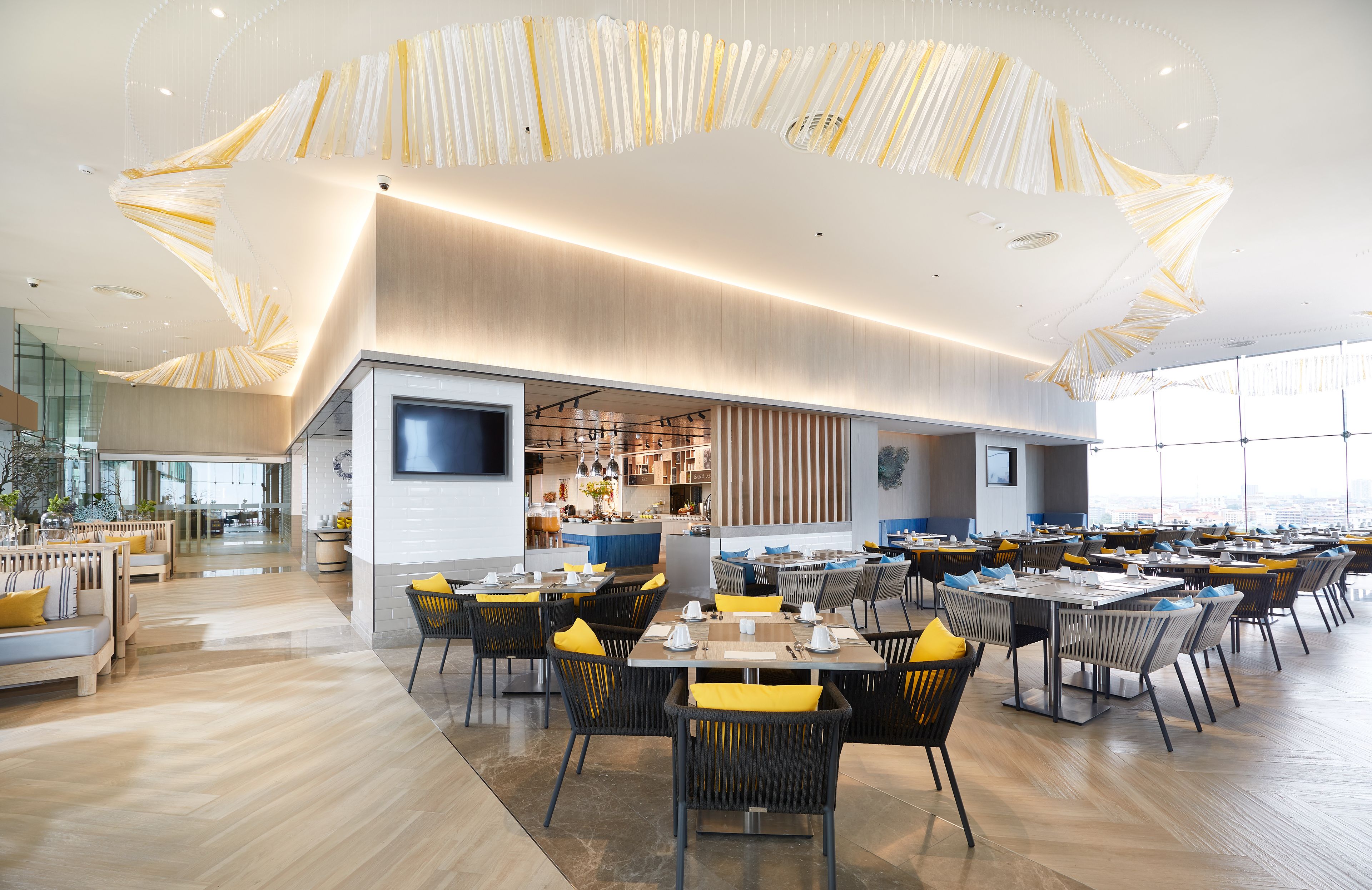 Un restaurante moderno con techo alto y luz natural, que ofrece diferentes opciones de asientos y una cocina a la vista.