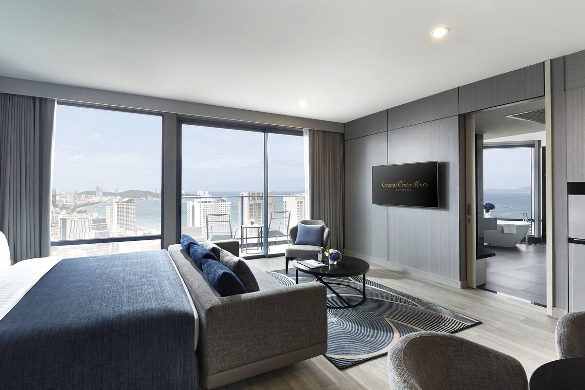 A modern hotel room with a large bed, a seating area, a flat-screen TV, and a city view.