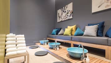 A spa room with a wooden bench, multiple bowls, and a sofa with cushions.