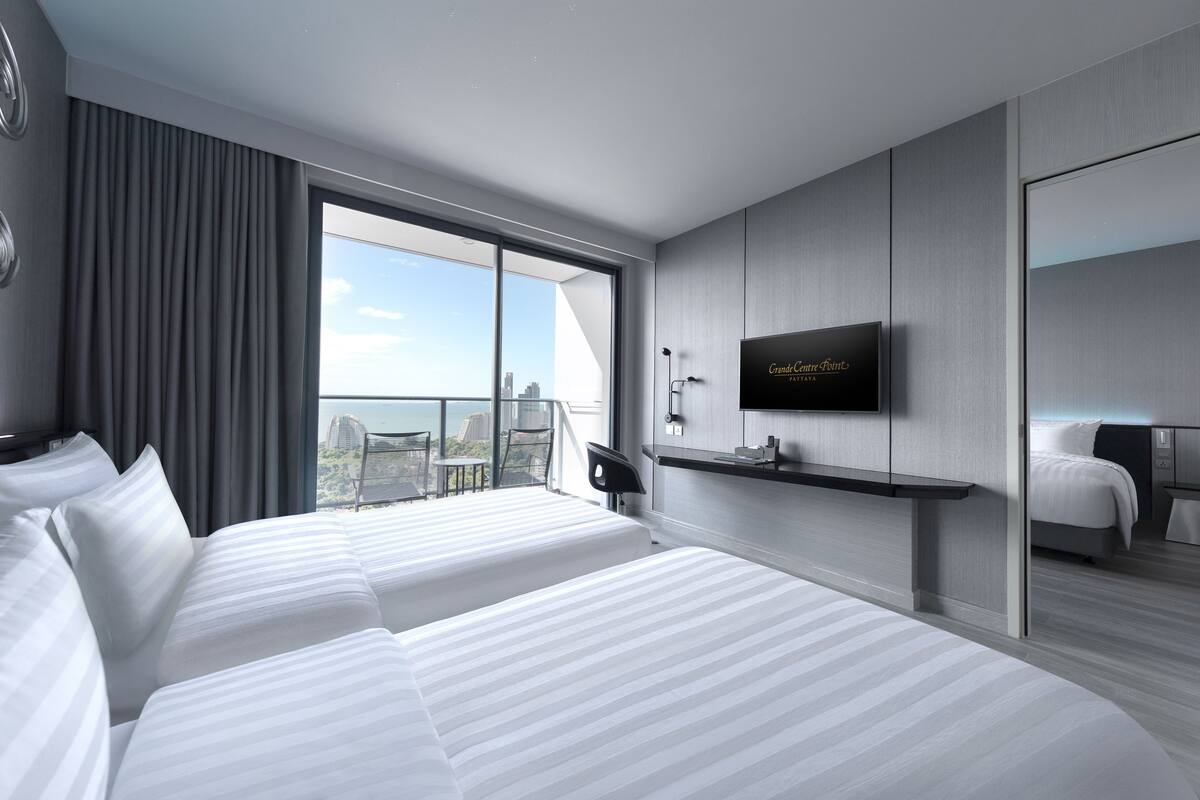 A modern hotel room with two beds, a TV, and a balcony with a city view.