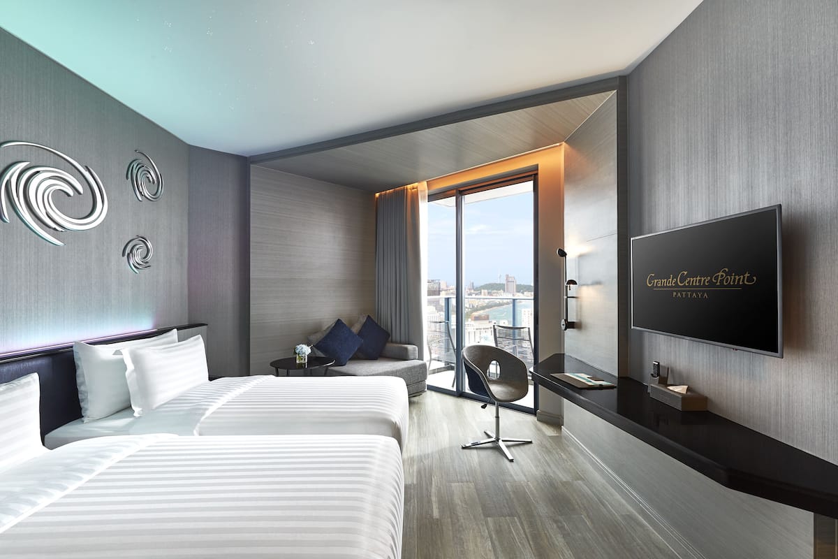A modern hotel room with a large bed, a sofa, a TV, and a balcony with a city view.