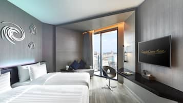 A modern hotel room with a large bed, a sofa, a TV, and a balcony with a city view.