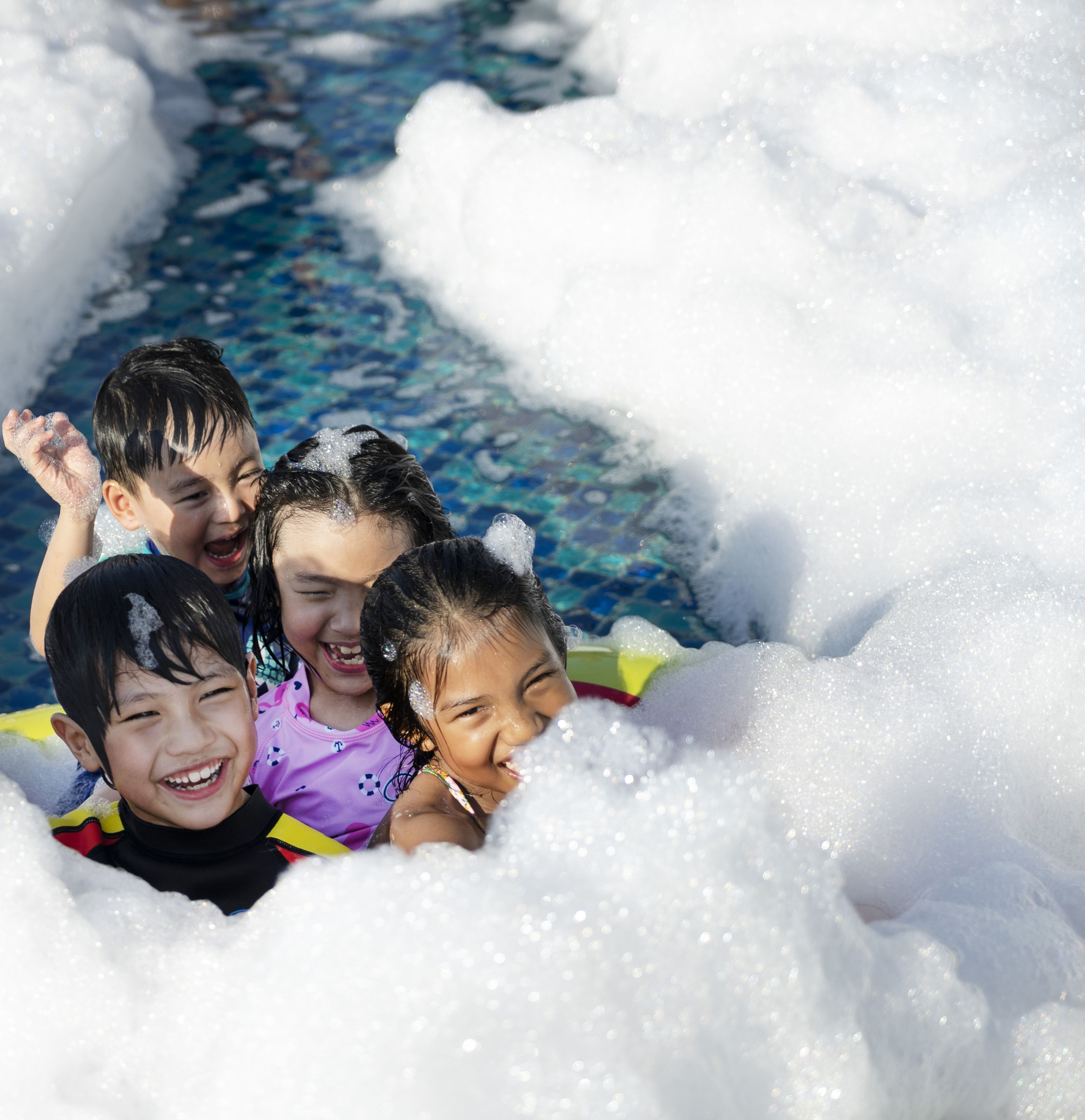Niños jugando en una piscina con agua y espuma.