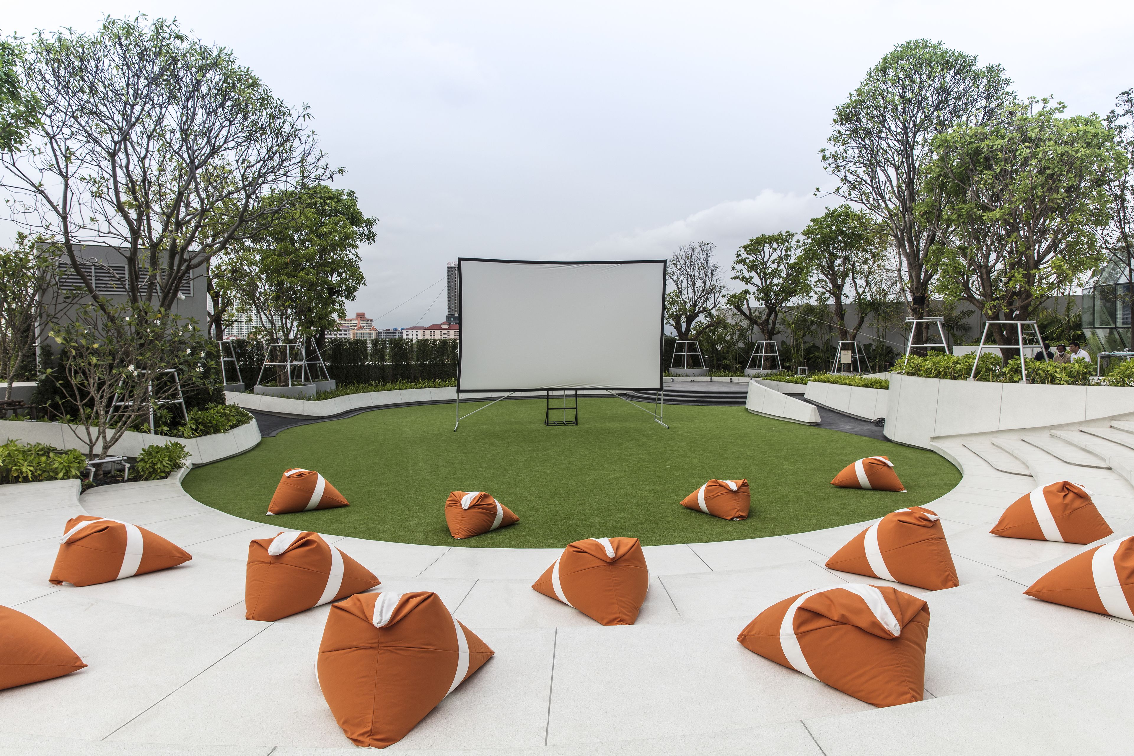 Un espace extérieur aménagé avec des sièges, doté d’un écran blanc et entouré de poufs orange et de verdure.
