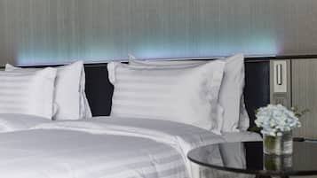 A modern hotel room with a neatly made bed, a bedside table with a vase of flowers, and a wall-mounted control panel.