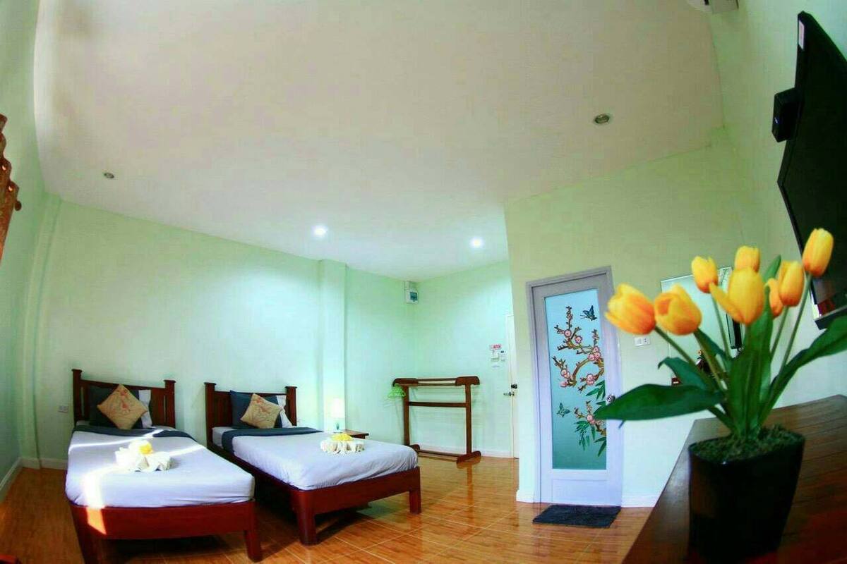 Quarto de hotel com duas camas de solteiro, um banco de madeira, uma planta em vaso e uma porta com design floral.
