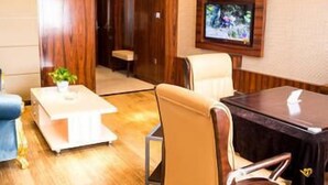 Ein Hotelzimmer mit Holzboden, einer weißen Couch, einem beigefarbenen Sessel, einem kleinen Tisch und einem an der Wand befestigten Fernseher.