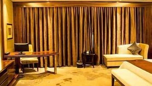 Ein Zimmer mit einer Couch, einem Couchtisch, einem Schreibtisch mit Stuhl und einem großen Fenster mit Vorhängen.