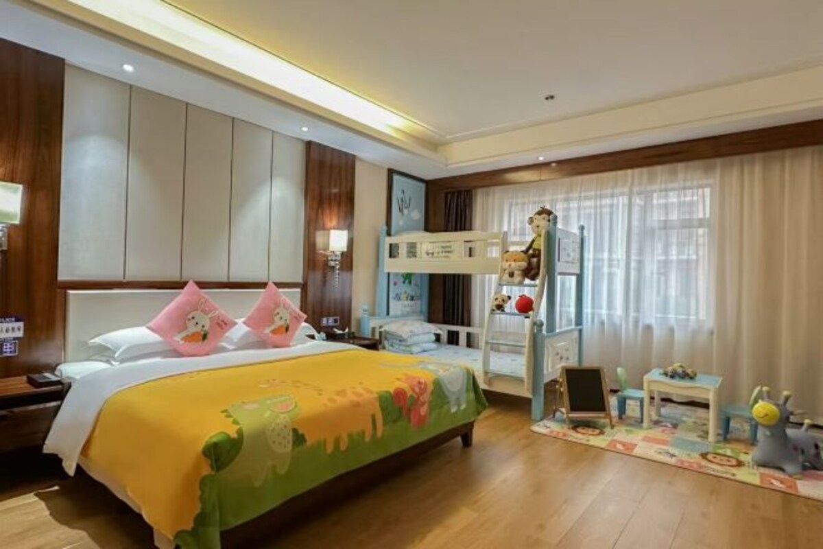 A hotel room with a bed, a bunk bed, a desk, and a window with curtains.