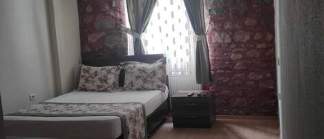 A bedroom with a bed, a bedside table, a lamp, and a window with curtains.