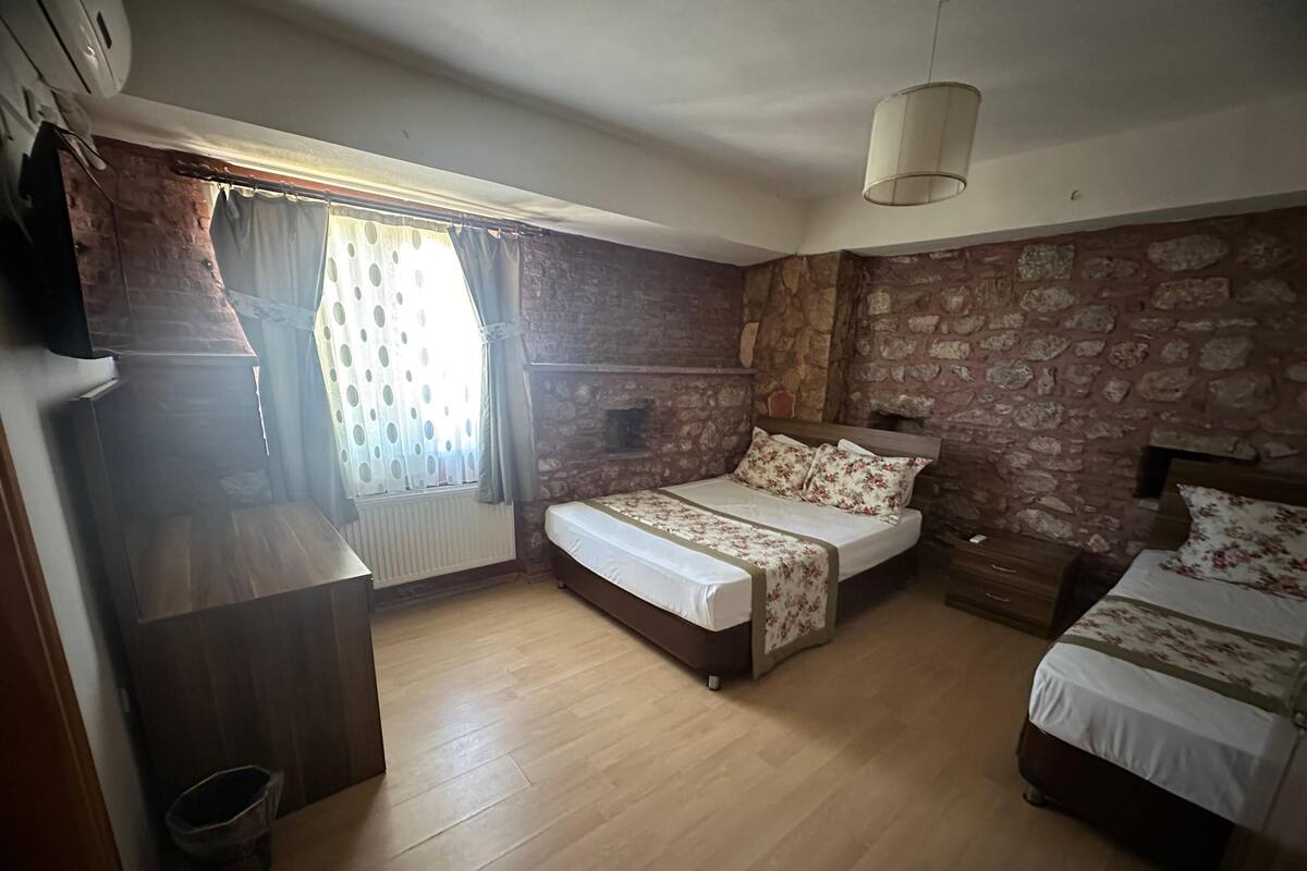 A bedroom with a stone wall, a wooden floor, a bed with floral bedding, a bedside table, and a hanging light fixture.