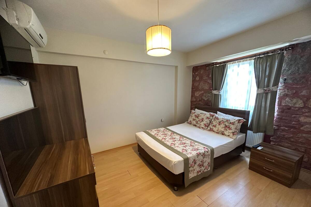 A bedroom with a wooden bed, a bedside table, a wardrobe, and a window with curtains.