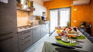 A modern kitchen with a dining area, featuring a gas stove, oven, and a dining table set with breakfast items. - B&B Pepito (Cefalù)
