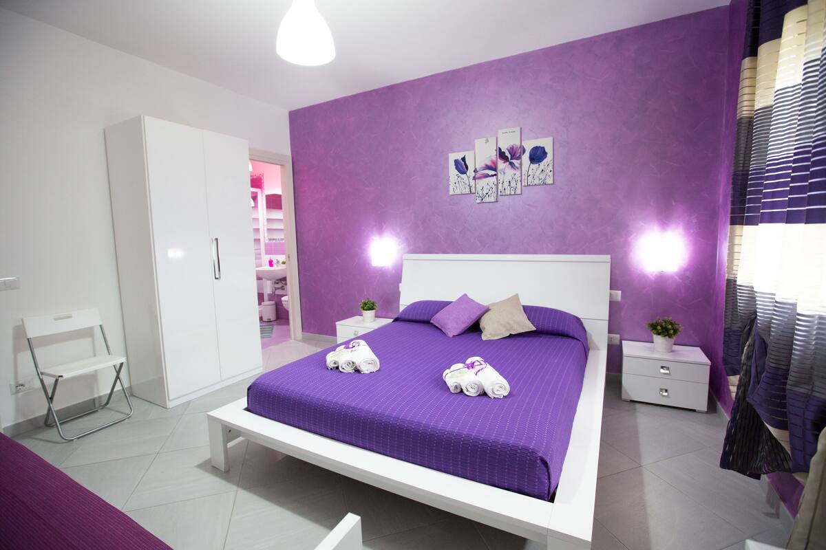 Un dormitorio con una cama grande, un armario blanco y un pequeño banco.