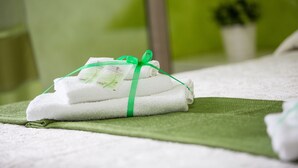 A neatly folded white towel tied with a green ribbon, placed on a green towel on a bed. - B&B Pepito (Cefalù)