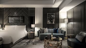 A modern hotel room with a large bed, a sofa, a coffee table, and a desk with a lamp.
