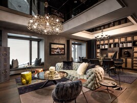 Un salon moderne avec un grand lustre, un ensemble de canapés, une table basse et une bibliothèque.