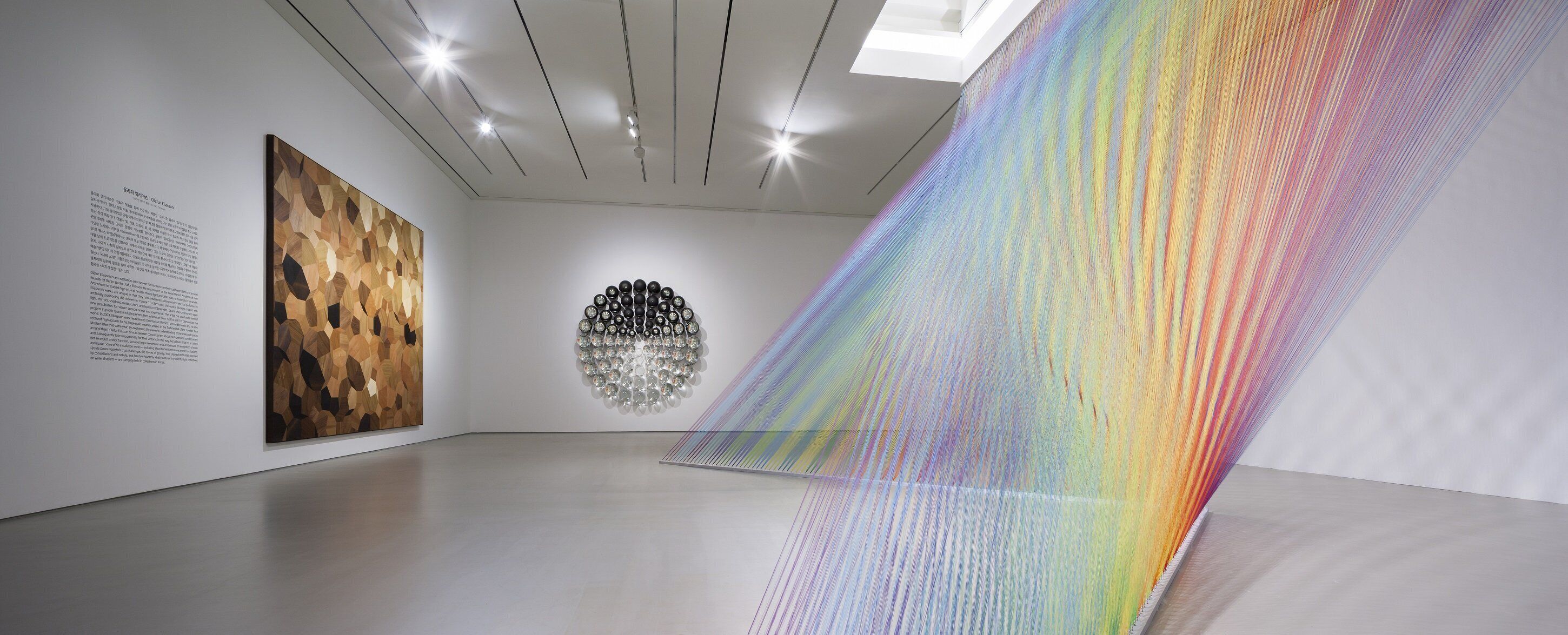 Una galería de arte con una obra geométrica en la pared, un panel de texto e instalación colorida.