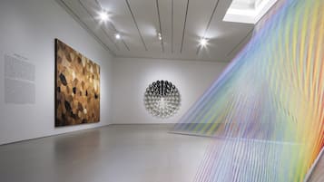 Una galería de arte con una obra geométrica en la pared, un panel de texto e instalación colorida.