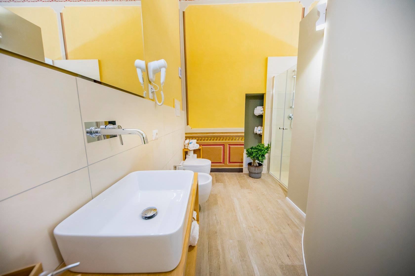 A narrow bathroom with a white sink, a mirror, and a hairdryer mounted on the wall.