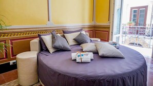 A room with a large bed, a round bedside table, and a window with a view of a balcony. - Pepito Palace (Cefalù)