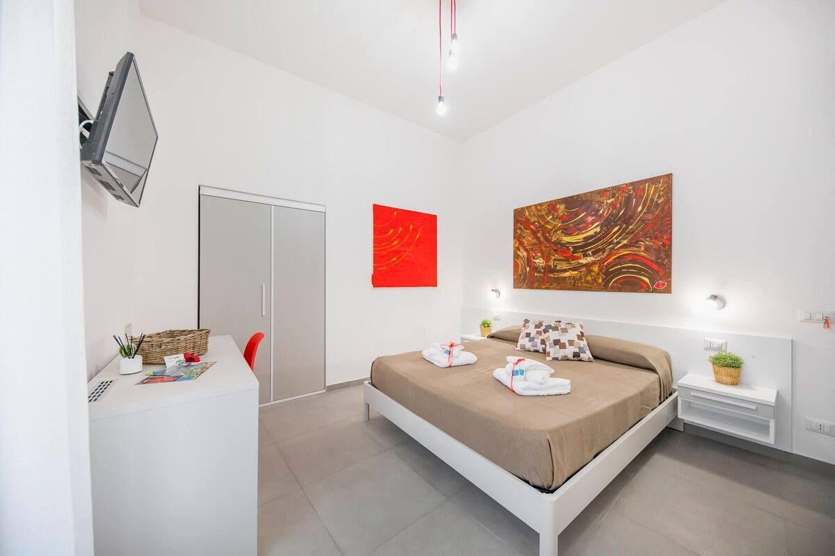 Een moderne hotelkamer met een bed, nachtkastje en bureau met stoel.