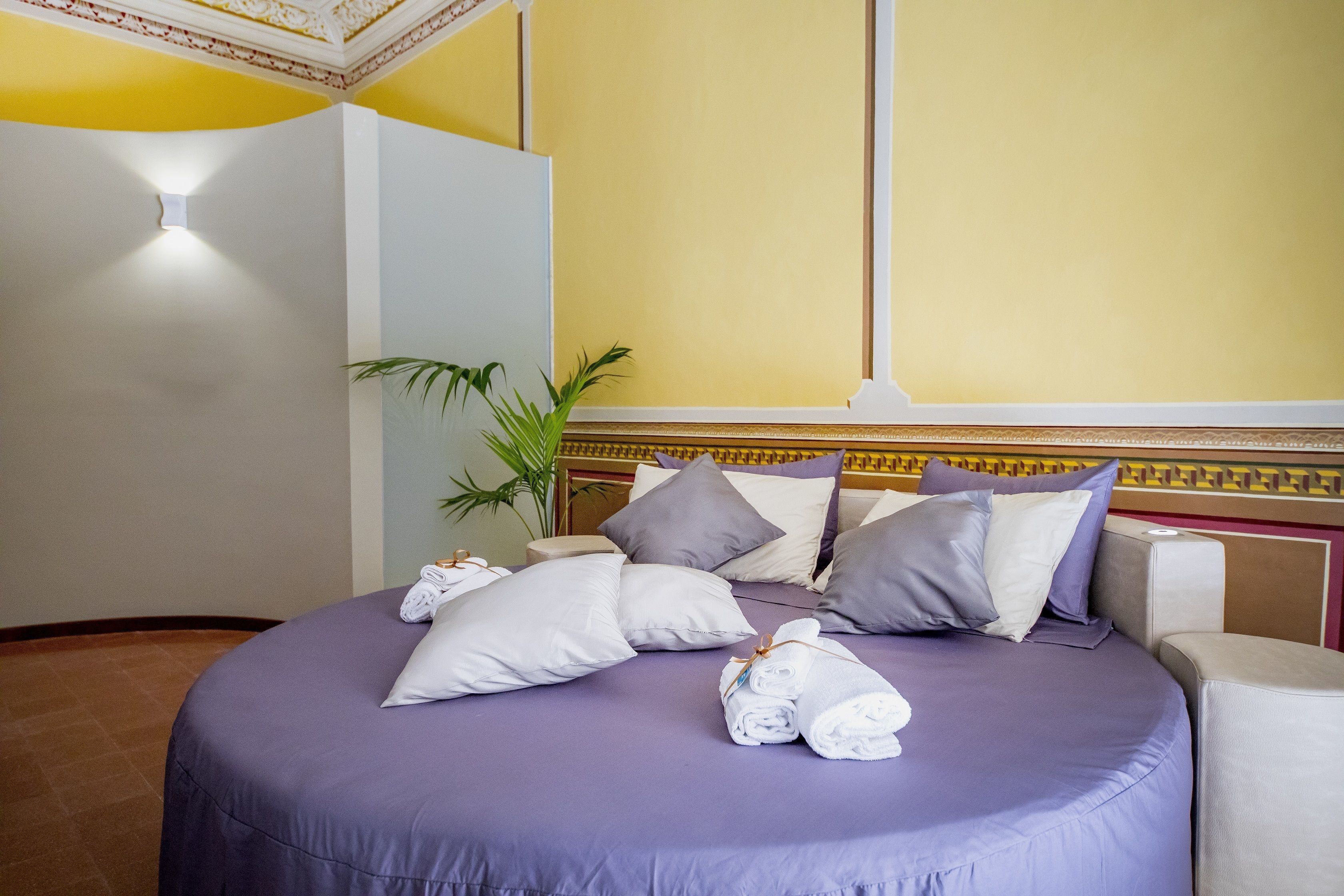 Un letto rifatto con una coperta viola, diversi cuscini e asciugamani arrotolati.
