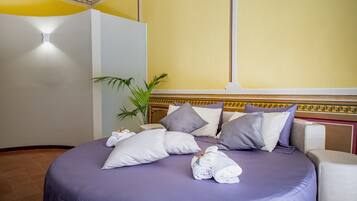 Un letto rifatto con una coperta viola, diversi cuscini e asciugamani arrotolati.