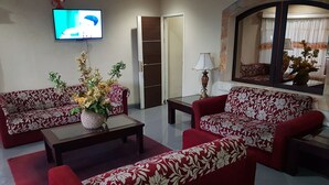 A living room with two red sofas, a coffee table, and a TV on the wall. - Hotel Scarlet Bukit Pakar (Bandung)