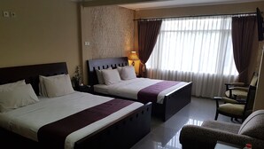 A hotel room with two beds, a sofa, a chair, and a table with a tray of water bottles and cups. - Hotel Scarlet Bukit Pakar (Bandung)