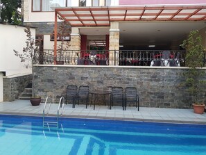 A poolside area with stone walls, metal chairs, and a covered seating area with umbrellas. - Hotel Scarlet Bukit Pakar (Bandung)