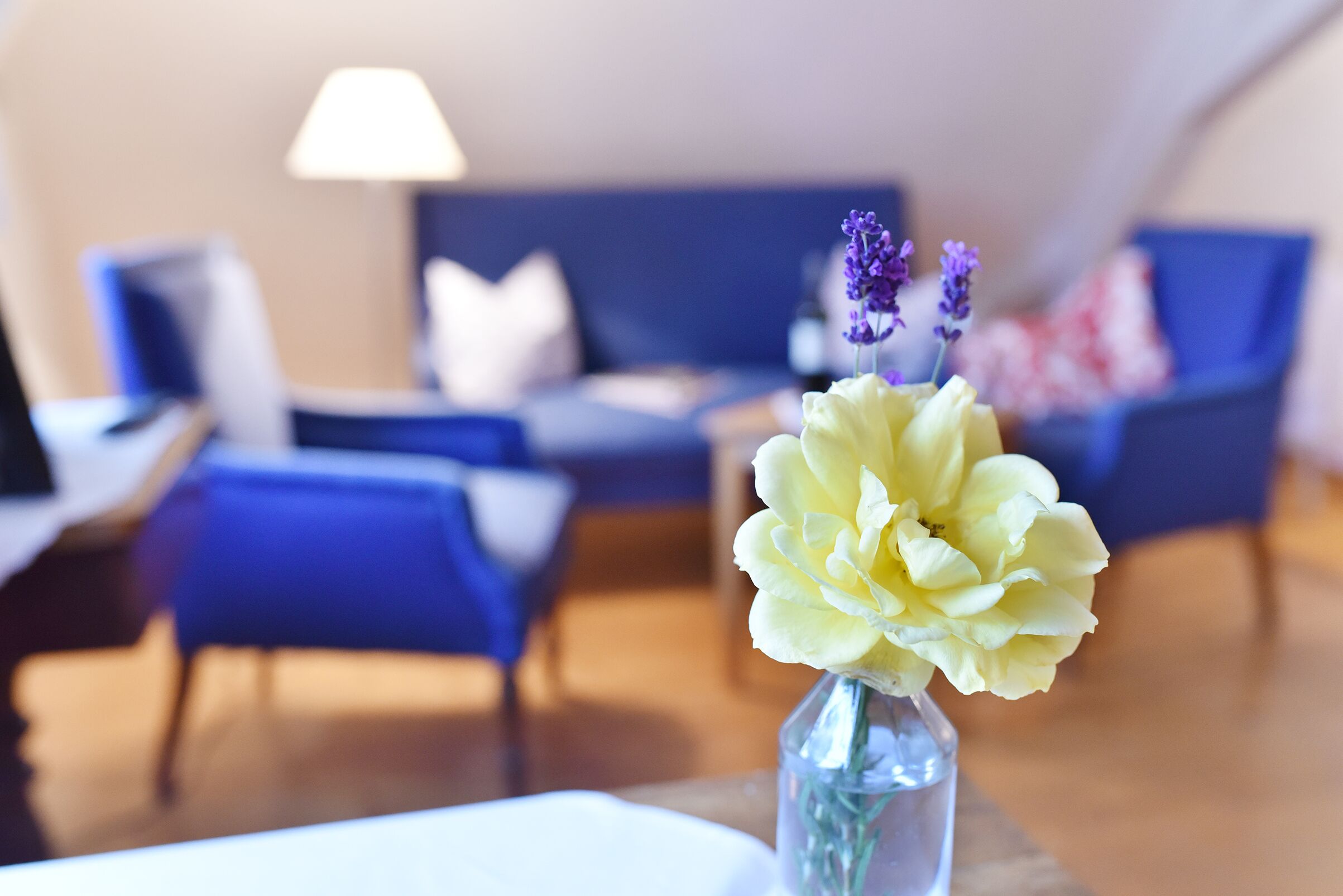 A modern living room with a blue sofa, a white table, and a vase with flowers.