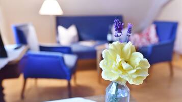A modern living room with a blue sofa, a white table, and a vase with flowers.
