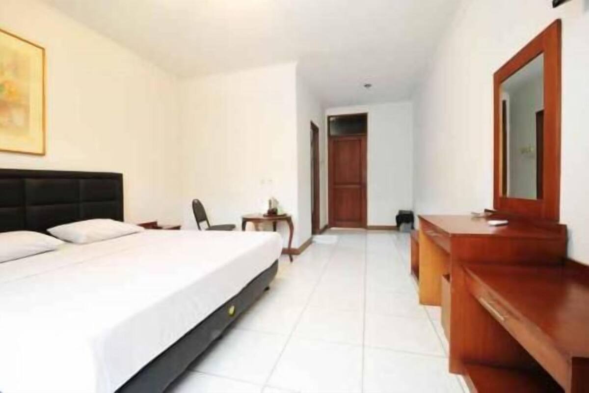 A hotel room with a bed, a desk, a chair, and a mirror.