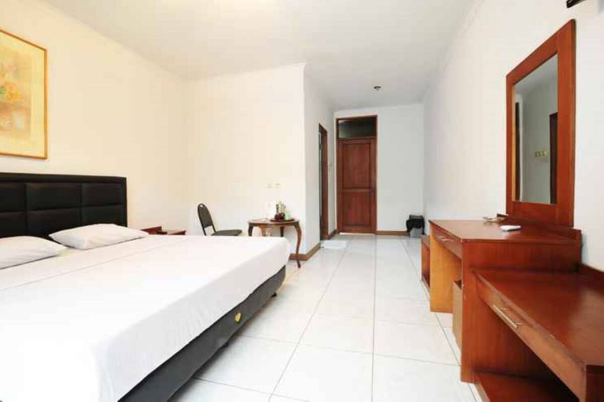 A hotel room with a bed, a wooden dresser, a mirror, a chair, and a small table.