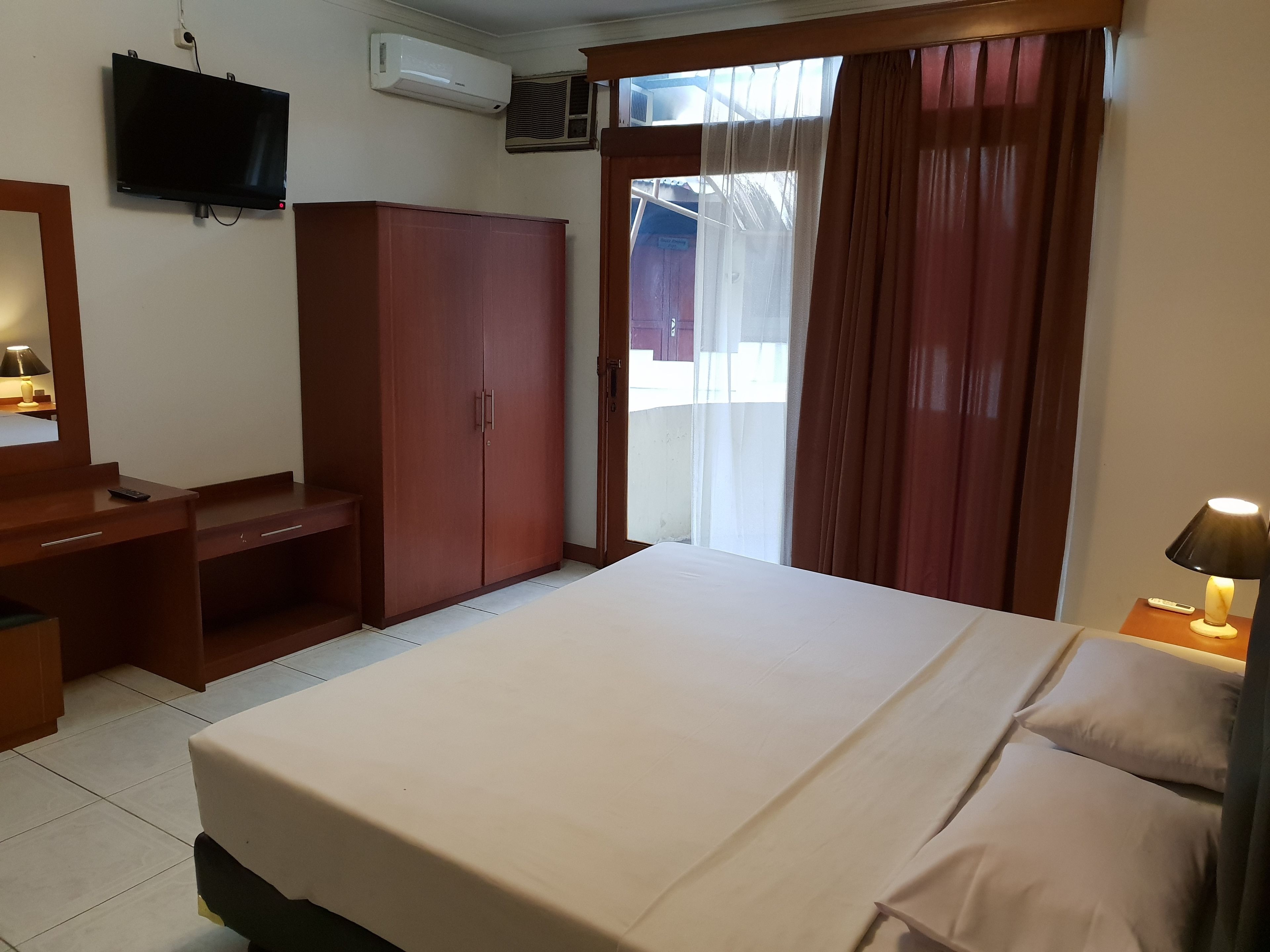 A hotel room with a bed, a desk, a wardrobe, a TV, and a window with curtains.