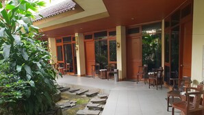 A covered outdoor area with stone steps leading to a seating area with wooden chairs and tables. - Hotel Dequr Bandung (Bandung)