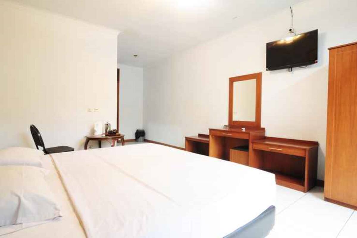 A hotel room with a large bed, a wooden dresser, a mirror, a television mounted on the wall, and a small table with a chair.
